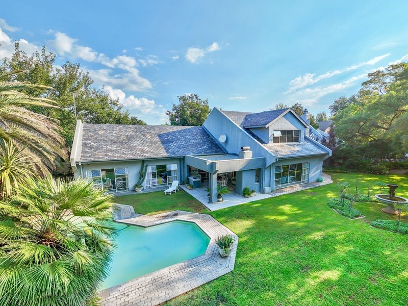 Aerial view of the rear elevation featuring a swimming pool, paved patio area, covered outdoor space, and a well-maintained garden.