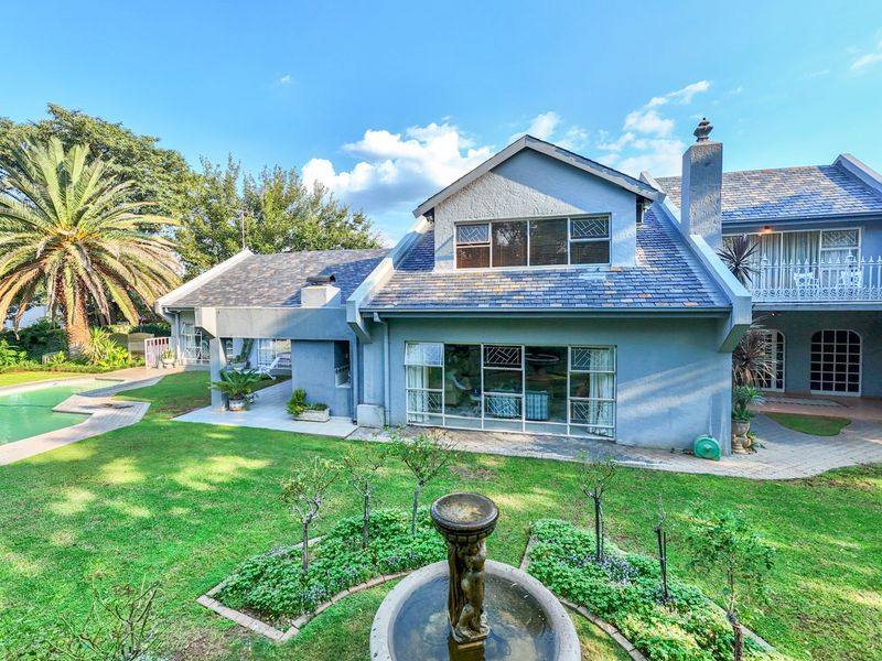 Rear view of the house featuring a slate roof, covered patio, swimming pool, and a landscaped garden with a central fountain.