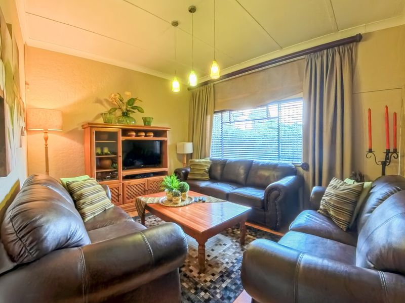 A comfortable living room featuring coved ceilings, pendant lighting, and large windows with venetian blinds and curtain tracks.
