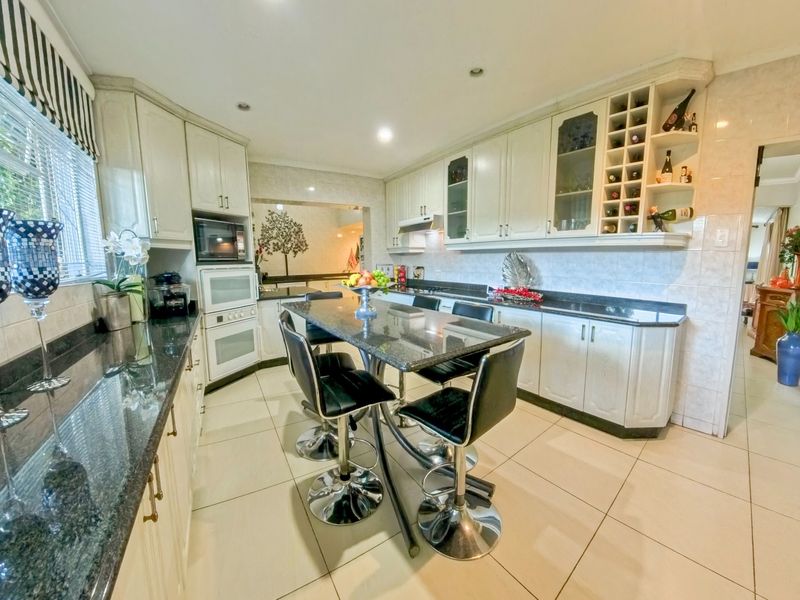 Spacious kitchen featuring granite countertops, built-in appliances, ample cabinetry with integrated wine storage, and neutral tiled flooring.