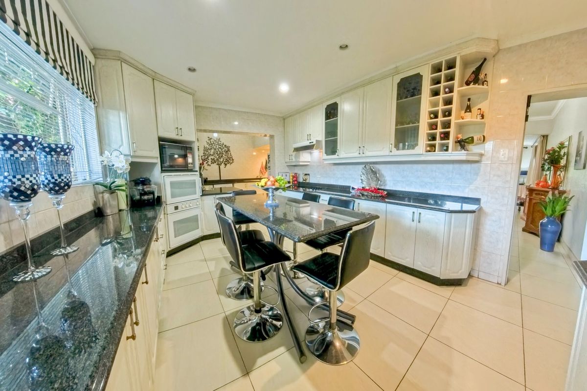 Spacious kitchen featuring granite countertops, built-in appliances, ample cabinetry with integrated wine storage, and neutral tiled flooring.