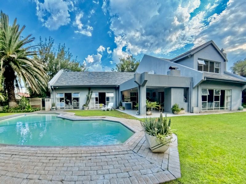 Rear view of the house featuring a swimming pool, paved surround, covered patio area, and a well-maintained garden.