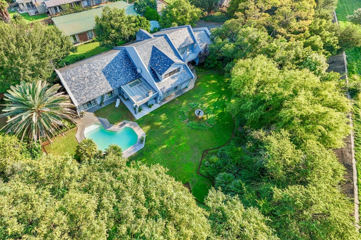 Aerial view of a residential property featuring a large landscaped garden, swimming pool, and a multi-level house with a tiled roof.