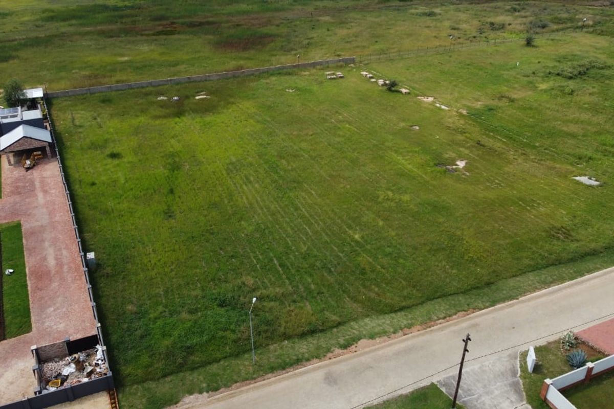 Aerial view of a vacant residential plot featuring a grassed surface, boundary wall, and adjacent paved driveway access.
