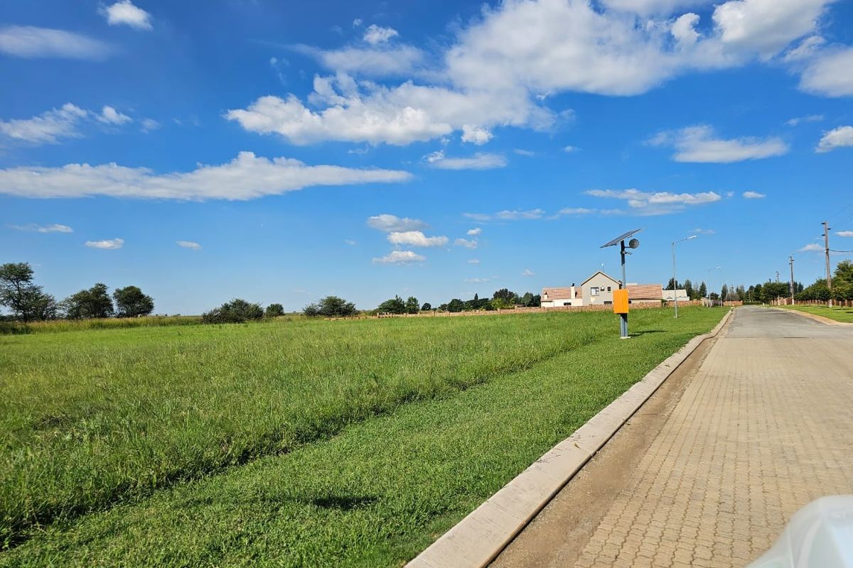 A view of a vacant residential plot featuring a paved road, concrete curbing, and a solar-powered street light.