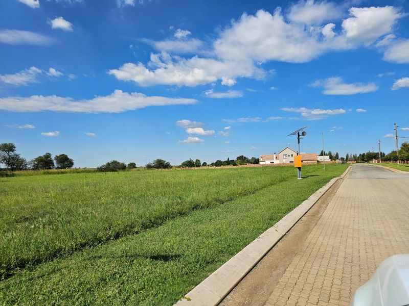 A view of a vacant residential plot featuring a paved road, concrete curbing, and a solar-powered street light.