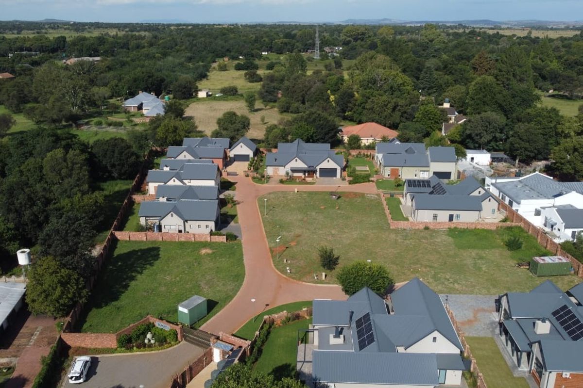Aerial view of a residential estate featuring multiple homes with metal roofs, solar panels, paved access roads, and established boundary walls.