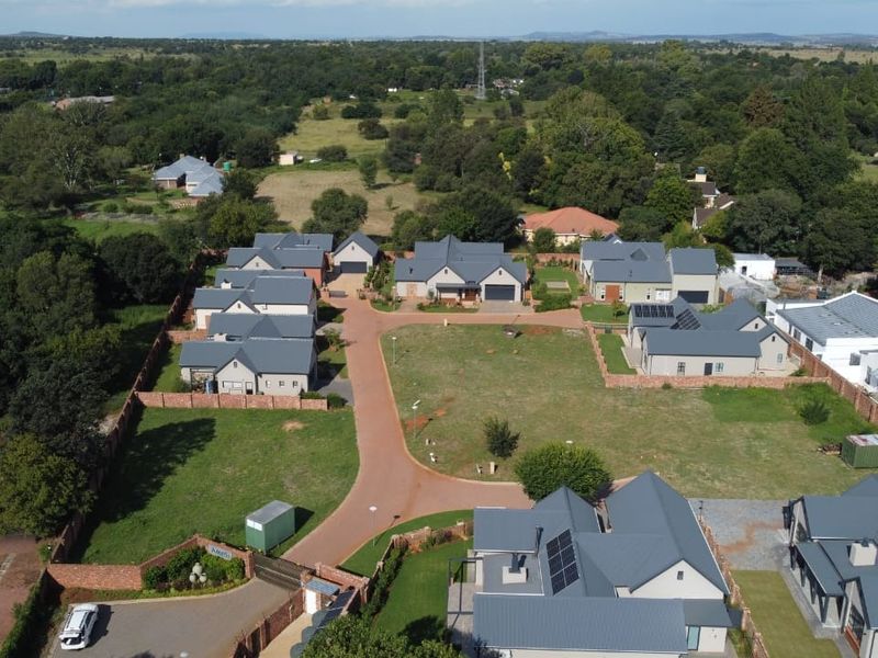 Aerial view of a residential estate featuring multiple homes with metal roofs, solar panels, paved access roads, and established boundary walls.
