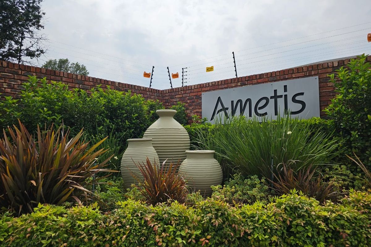 A well-maintained estate entrance featuring a brick boundary wall, electric security fencing, and professional landscaping with decorative urns.