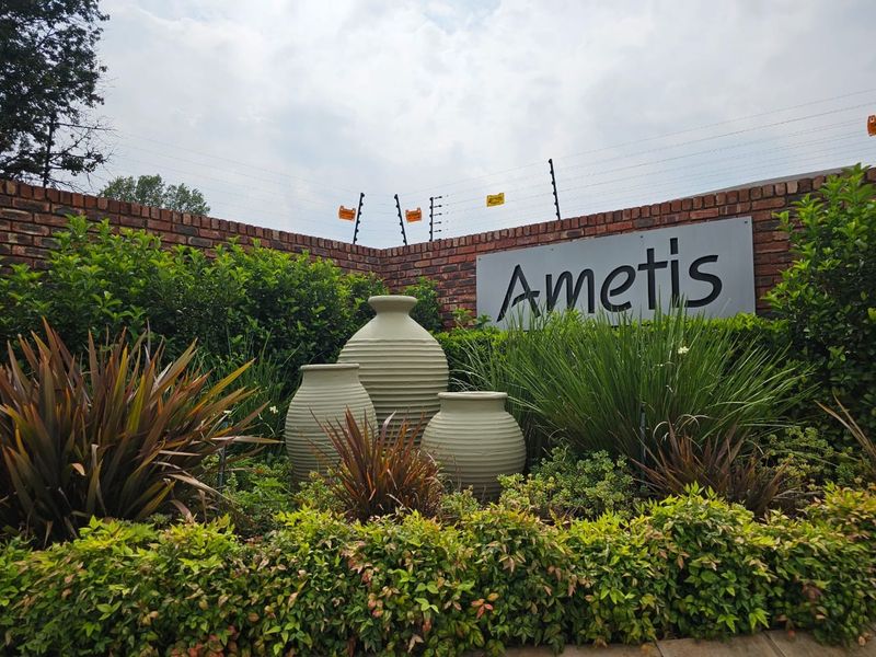 A well-maintained estate entrance featuring a brick boundary wall, electric security fencing, and professional landscaping with decorative urns.