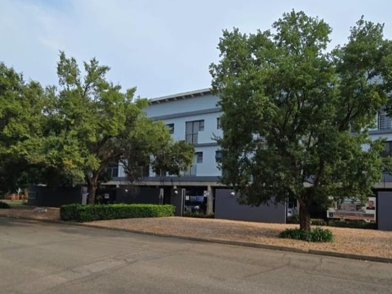 Front elevation of a multi-story apartment complex featuring modern grey facade, private balconies, and established trees along the street boundary.