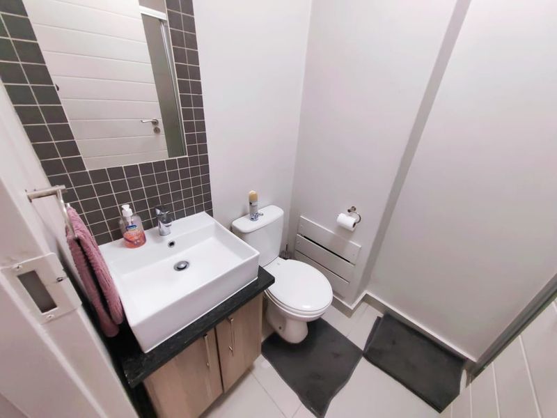 A compact, modern bathroom featuring a vanity unit with a ceramic basin, a wall-mounted mirror, and a standard toilet with tiled finishes.