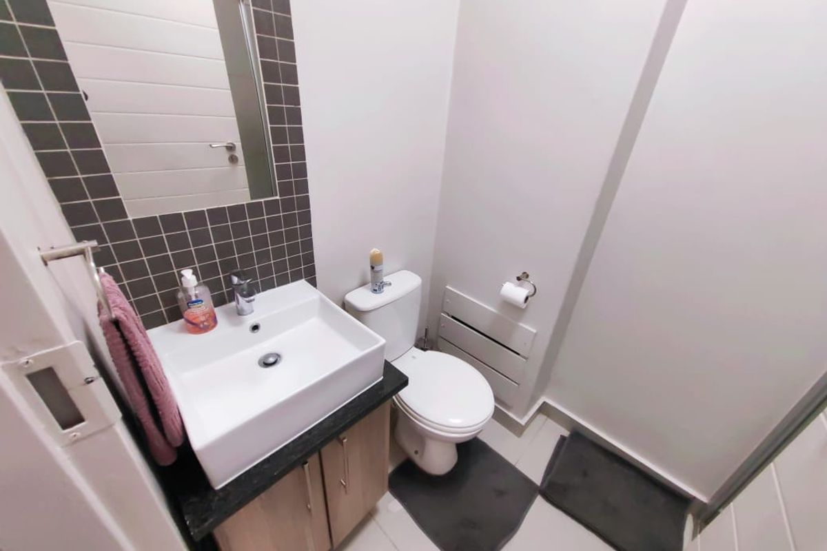 A compact, modern bathroom featuring a vanity unit with a ceramic basin, a wall-mounted mirror, and a standard toilet with tiled finishes.