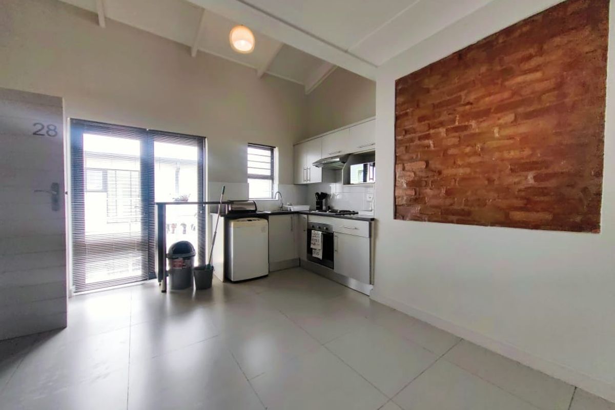 A compact kitchen featuring built-in cabinetry, integrated appliances, and a distinctive exposed brick feature wall, leading out to an exterior sliding door.
