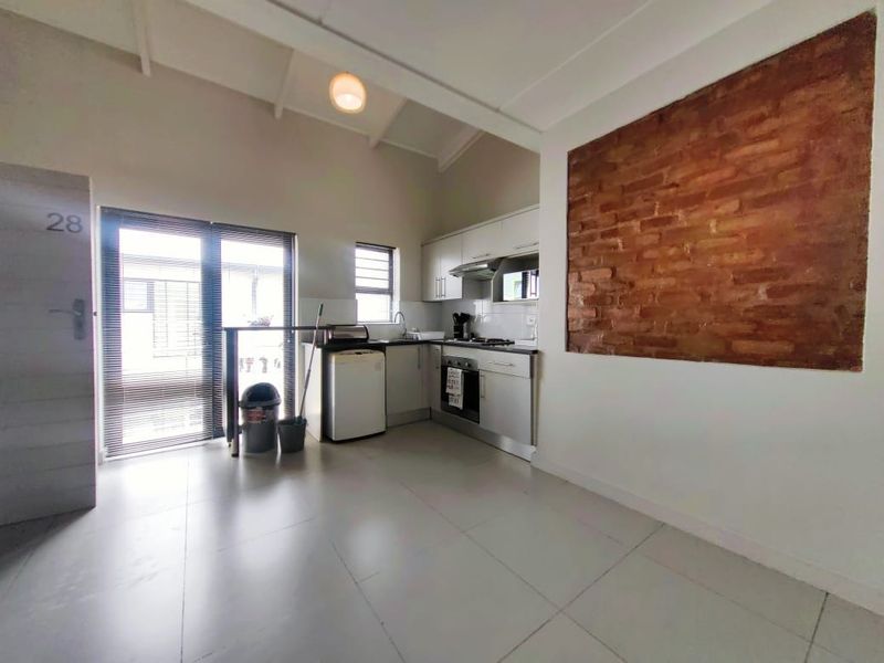 A compact kitchen featuring built-in cabinetry, integrated appliances, and a distinctive exposed brick feature wall, leading out to an exterior sliding door.