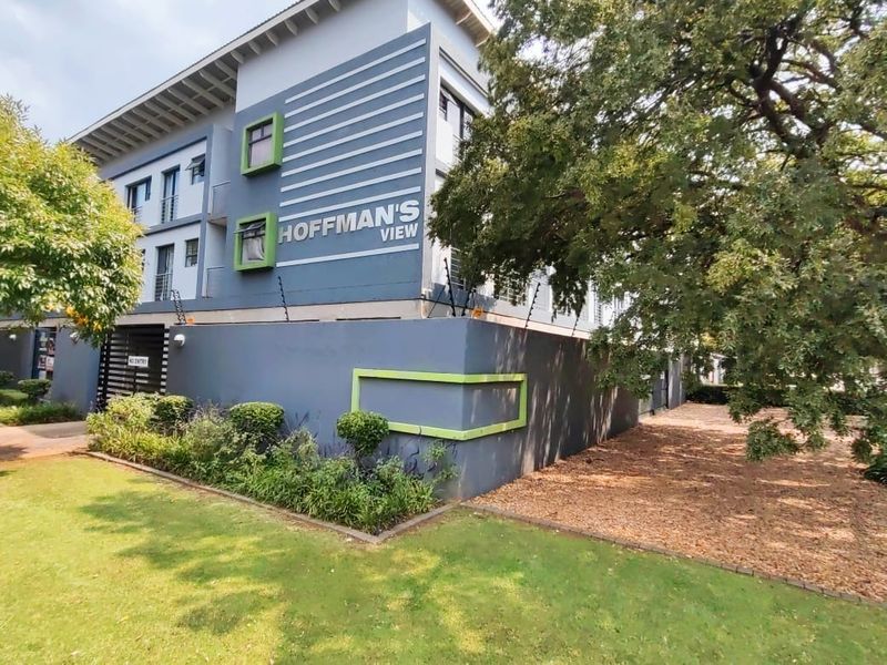 Exterior view of Hoffman's View apartment complex featuring modern grey facade, landscaped garden, and secure perimeter wall with electric fencing.