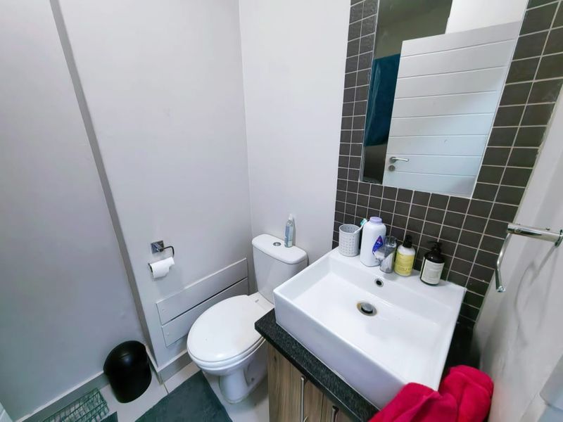 A compact bathroom featuring a modern basin with vanity storage, a tiled splashback, and a wall-mounted mirror.