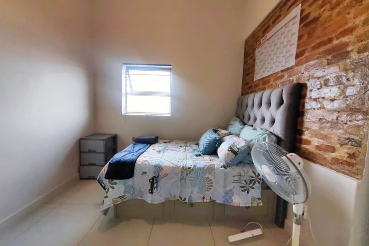 A bedroom featuring a rustic exposed brick feature wall, neutral tiled flooring, and a window providing natural light.