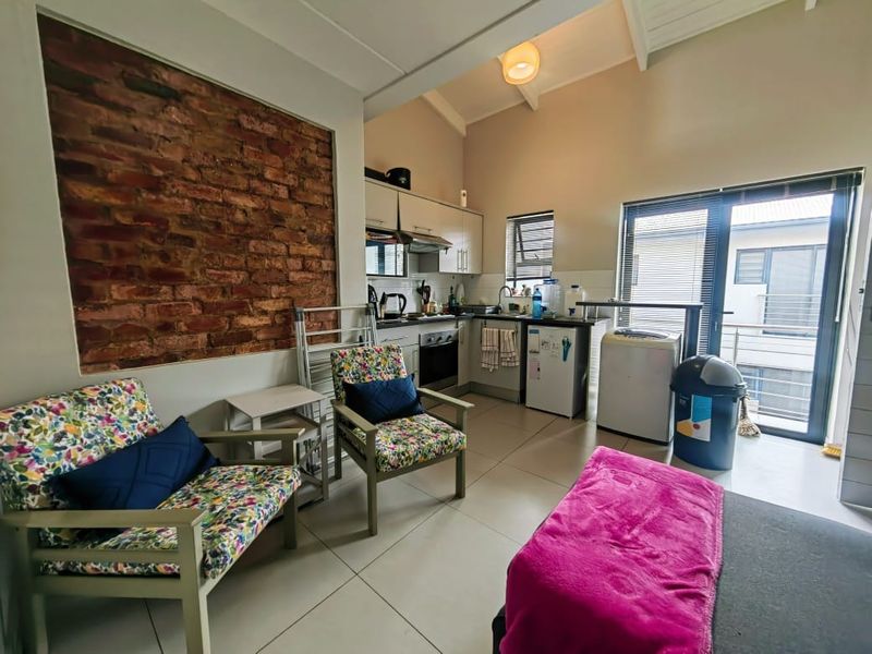 Open-plan living and kitchen area featuring an exposed brick wall, tiled floors, vaulted ceilings, and direct access to a balcony through sliding glass doors.