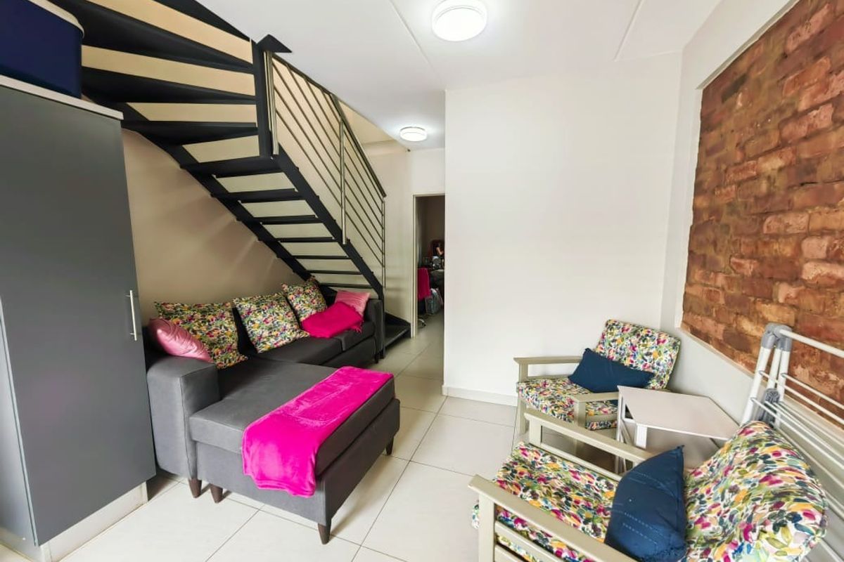 A living area featuring an exposed brick feature wall, tiled flooring, and a modern metal staircase leading to an upper level.