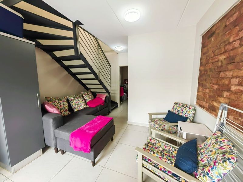 A living area featuring an exposed brick feature wall, tiled flooring, and a modern metal staircase leading to an upper level.