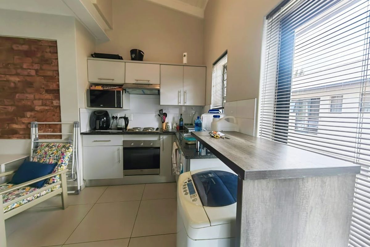 Compact kitchen featuring built-in cabinetry, electric oven and hob, breakfast bar, and an exposed brick feature wall with tiled flooring.