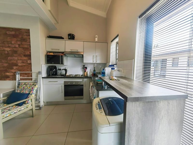 Compact kitchen featuring built-in cabinetry, electric oven and hob, breakfast bar, and an exposed brick feature wall with tiled flooring.
