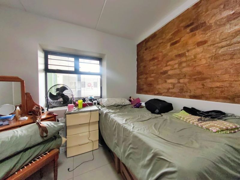 A bedroom featuring an exposed brick accent wall, tiled flooring, and a window with fitted venetian blinds.