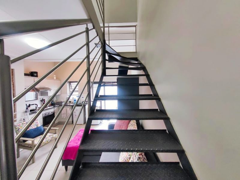 Open-plan living area featuring a modern metal staircase with stainless steel balustrades, overlooking a functional kitchen with built-in cabinetry and appliances.