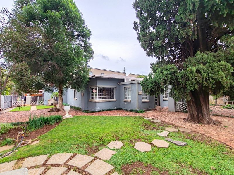 Front view of the property featuring a landscaped garden, brick paved pathways, and a secure entrance with established trees.