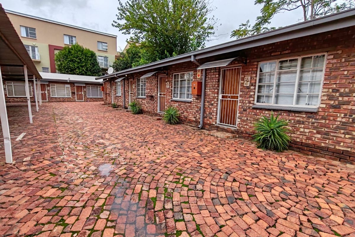 Exterior view of a brick residential complex featuring a cobblestone courtyard, security gates, and covered parking structures.