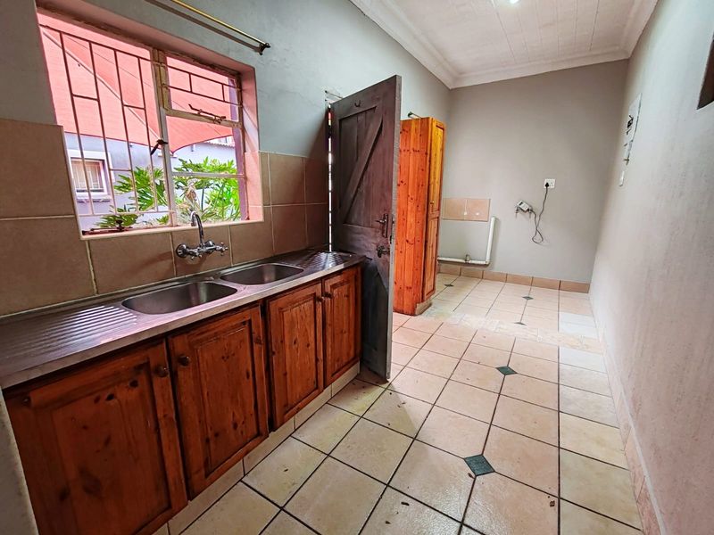 A functional laundry area featuring tiled flooring, timber cabinetry, and a double stainless steel sink with plumbing connections for appliances.