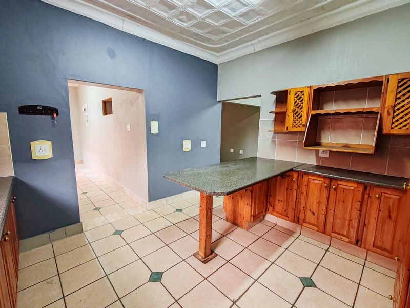 A functional kitchen featuring wooden cabinetry, granite countertops, a breakfast bar, and tiled flooring, with a distinctive pressed metal ceiling.