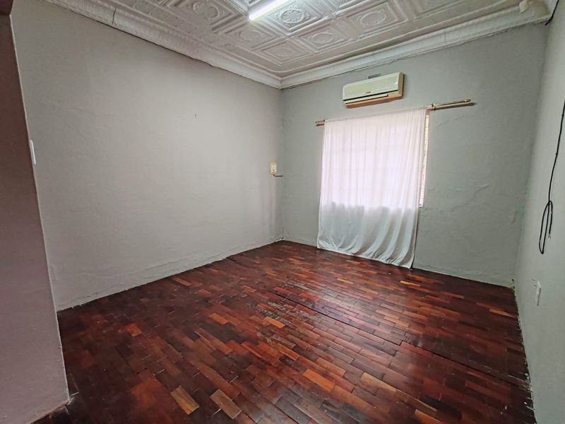 An empty bedroom featuring original parquet flooring, a decorative pressed metal ceiling, and a wall-mounted air conditioning unit.