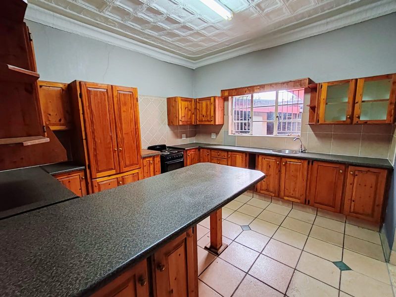 A spacious kitchen featuring wooden cabinetry, laminate countertops, a freestanding stove, and a unique pressed metal ceiling, offering a functional layout with ample storage.