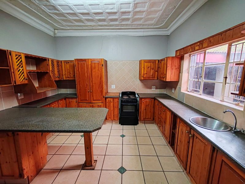 A spacious kitchen featuring wooden cabinetry, laminate countertops, a freestanding stove, and decorative ceiling tiles, offering a functional layout with potential for modernization.