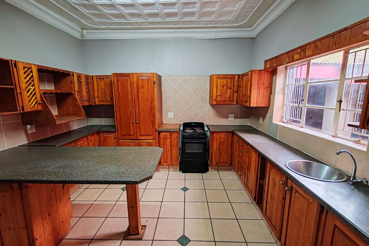 A spacious kitchen featuring wooden cabinetry, laminate countertops, a freestanding stove, and decorative ceiling tiles, offering a functional layout with potential for modernization.