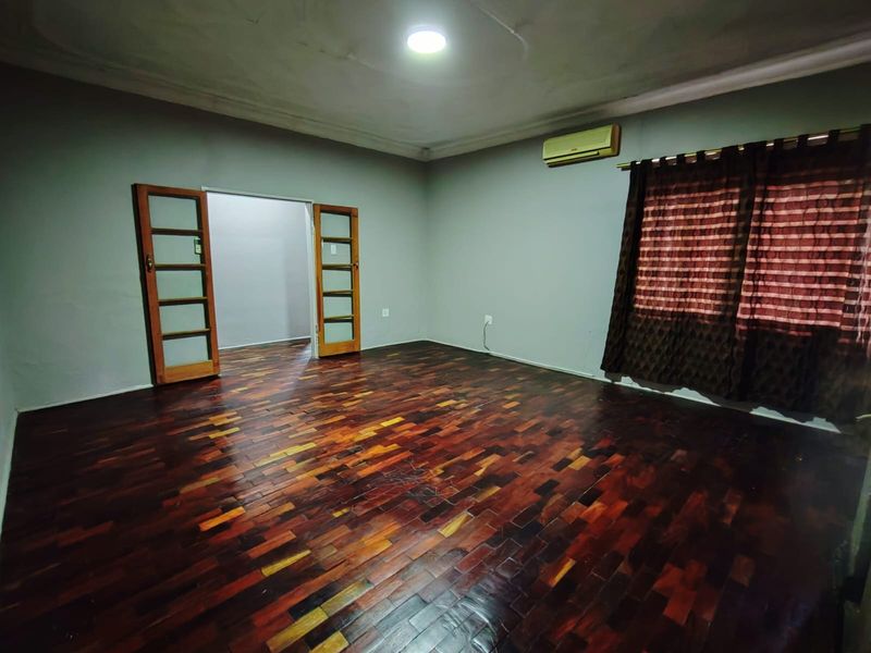 Spacious living room featuring polished parquet flooring, a wall-mounted air conditioning unit, and wooden framed glass doors leading to an adjacent room.