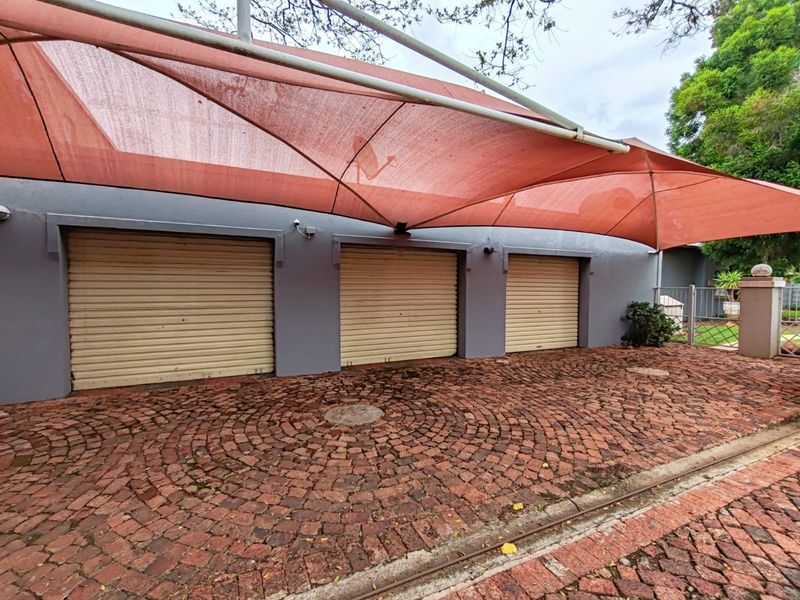 A triple garage featuring roll-up doors, a large overhead shade sail, and a decorative cobblestone driveway.