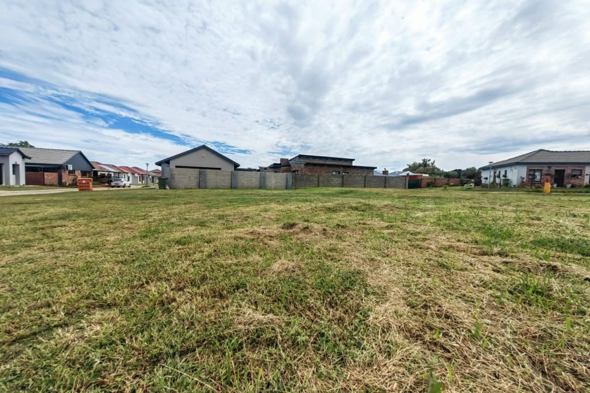 A vacant residential plot featuring a level grass lawn and established boundary walls, situated within a developed residential estate.