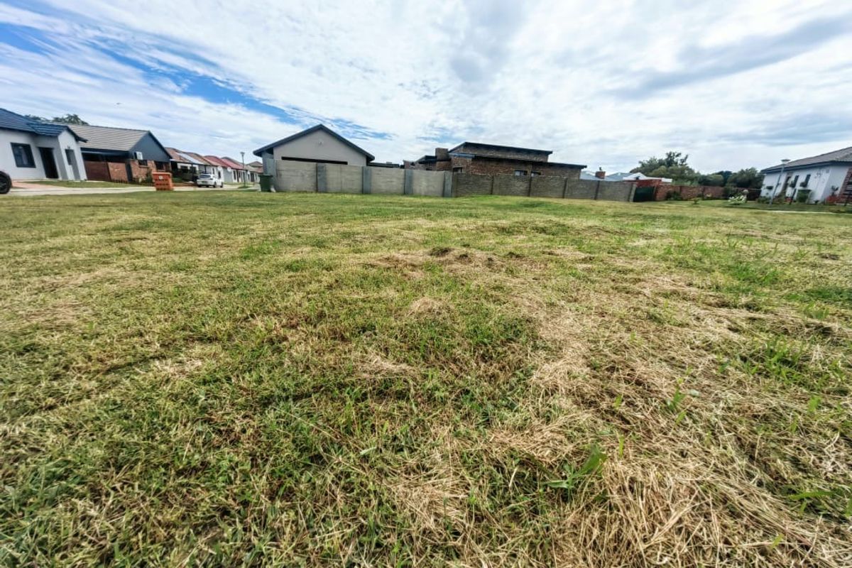 A vacant residential plot featuring a grass lawn and boundary wall, situated within a developed neighborhood setting.