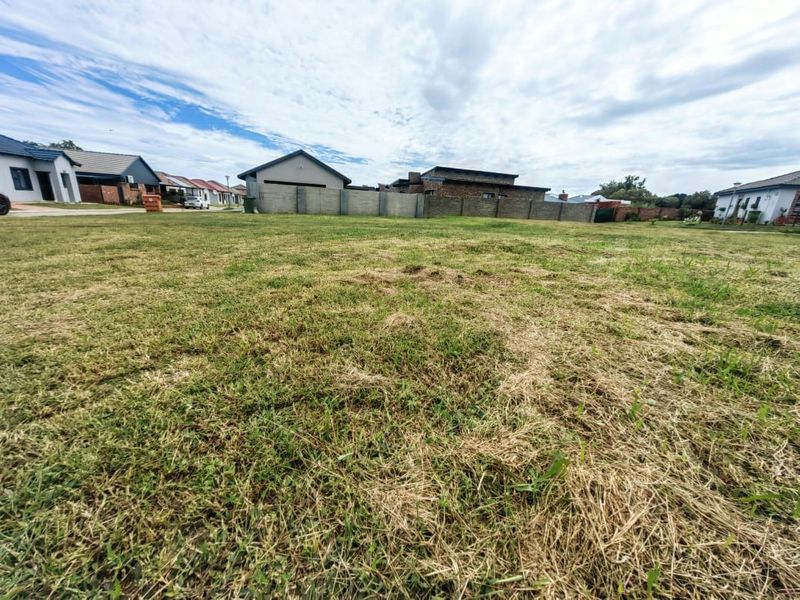 A vacant residential plot featuring a grass lawn and boundary wall, situated within a developed neighborhood setting.