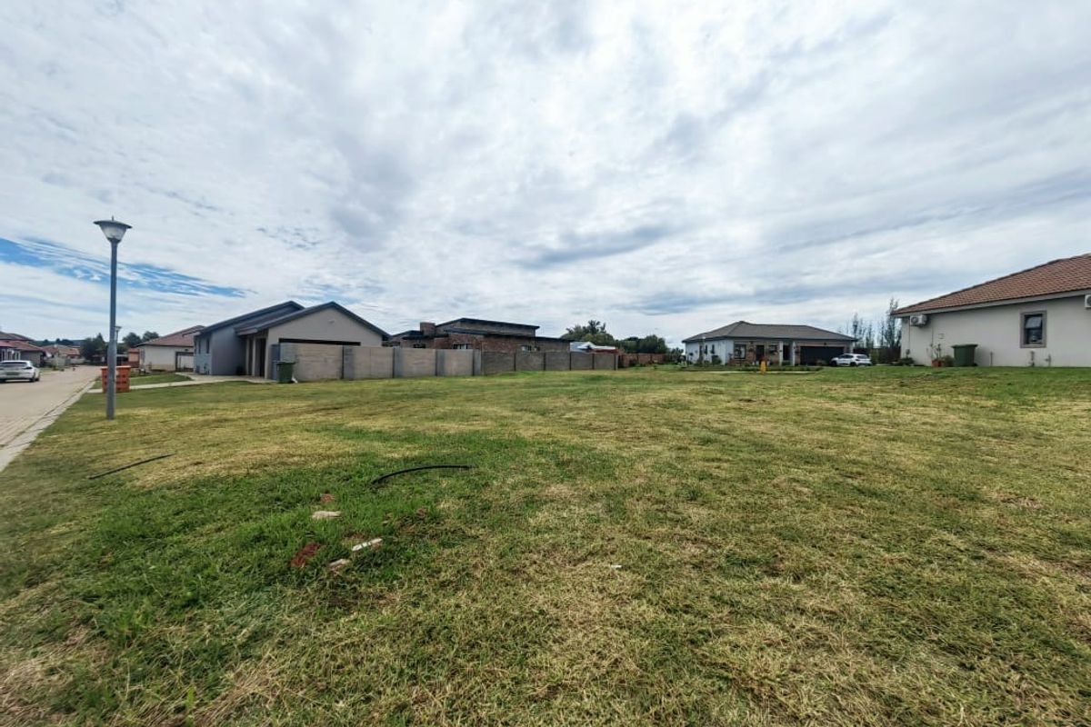 A vacant residential plot of land situated in a developed neighborhood, featuring a level grass surface and established boundary walls.