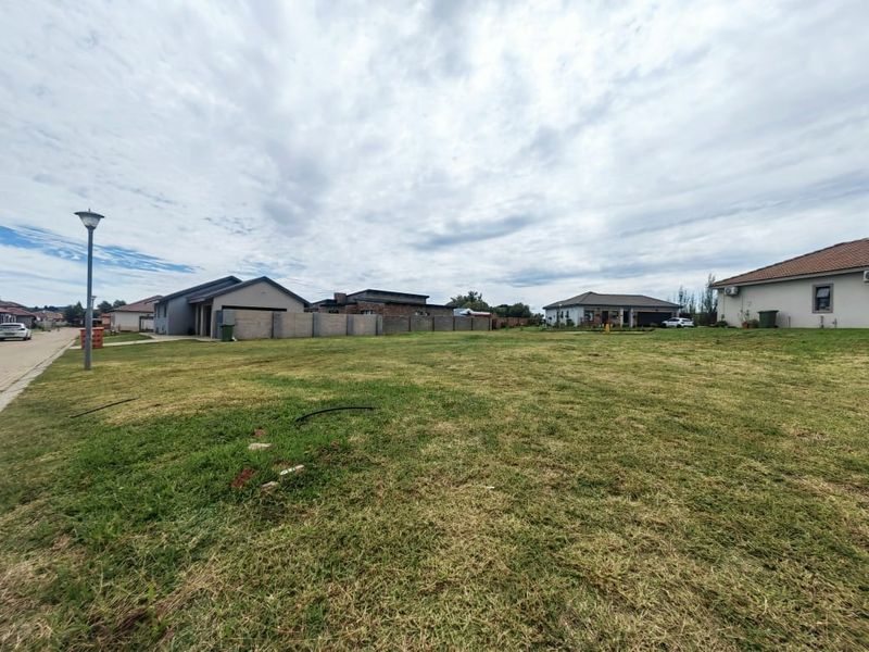 A vacant residential plot of land situated in a developed neighborhood, featuring a level grass surface and established boundary walls.