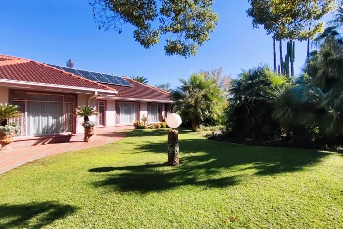 A well-maintained rear exterior view featuring a paved patio, lush landscaped garden, and a tiled roof equipped with solar panels.