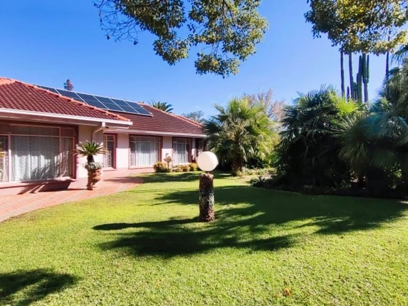 A well-maintained rear exterior view featuring a paved patio, lush landscaped garden, and a tiled roof equipped with solar panels.