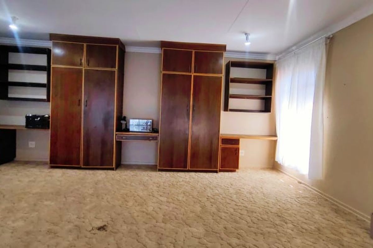 Spacious bedroom featuring extensive built-in cabinetry, integrated desk spaces, and shelving units, offering significant storage potential in a neutral setting.