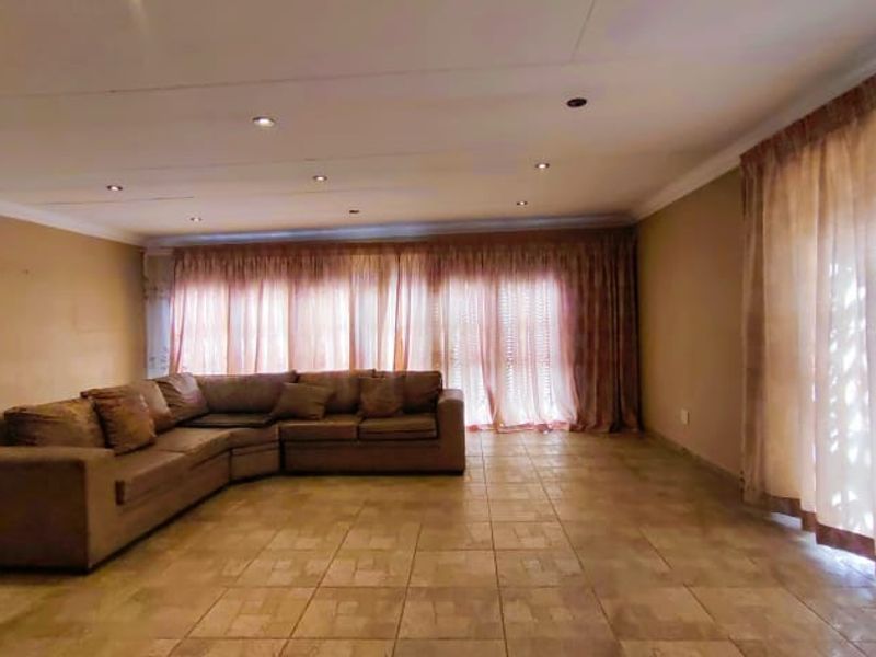 Spacious living area featuring tiled flooring, recessed downlighting, and large windows covered by floor-to-ceiling curtains.