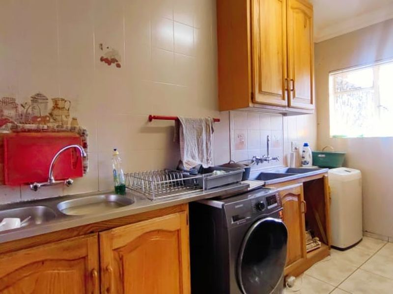 Functional laundry area featuring wooden cabinetry, double stainless steel sink, and tiled splashback, providing practical utility space for household chores.