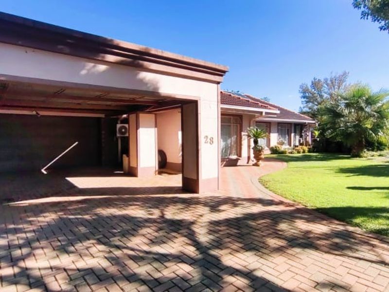 Front view of the property featuring a spacious paved driveway, covered carport, and a well-maintained landscaped garden.